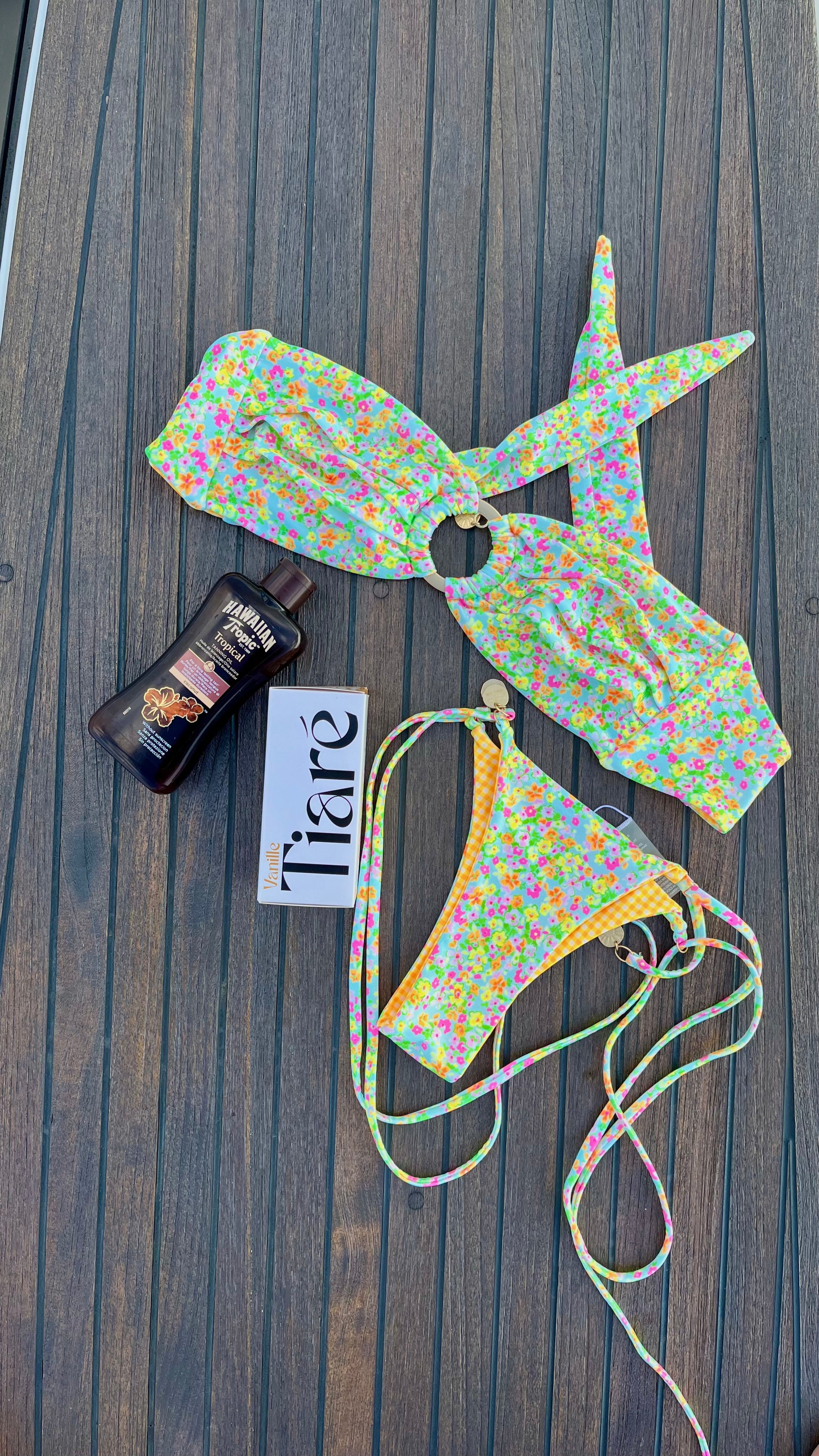 Eau de Toilette Tiare 100ml Verpackung auf einem Boot liegend. Daneben ein Bikini im Blumenmuster. links daneben eine Sonnenschutzflasche