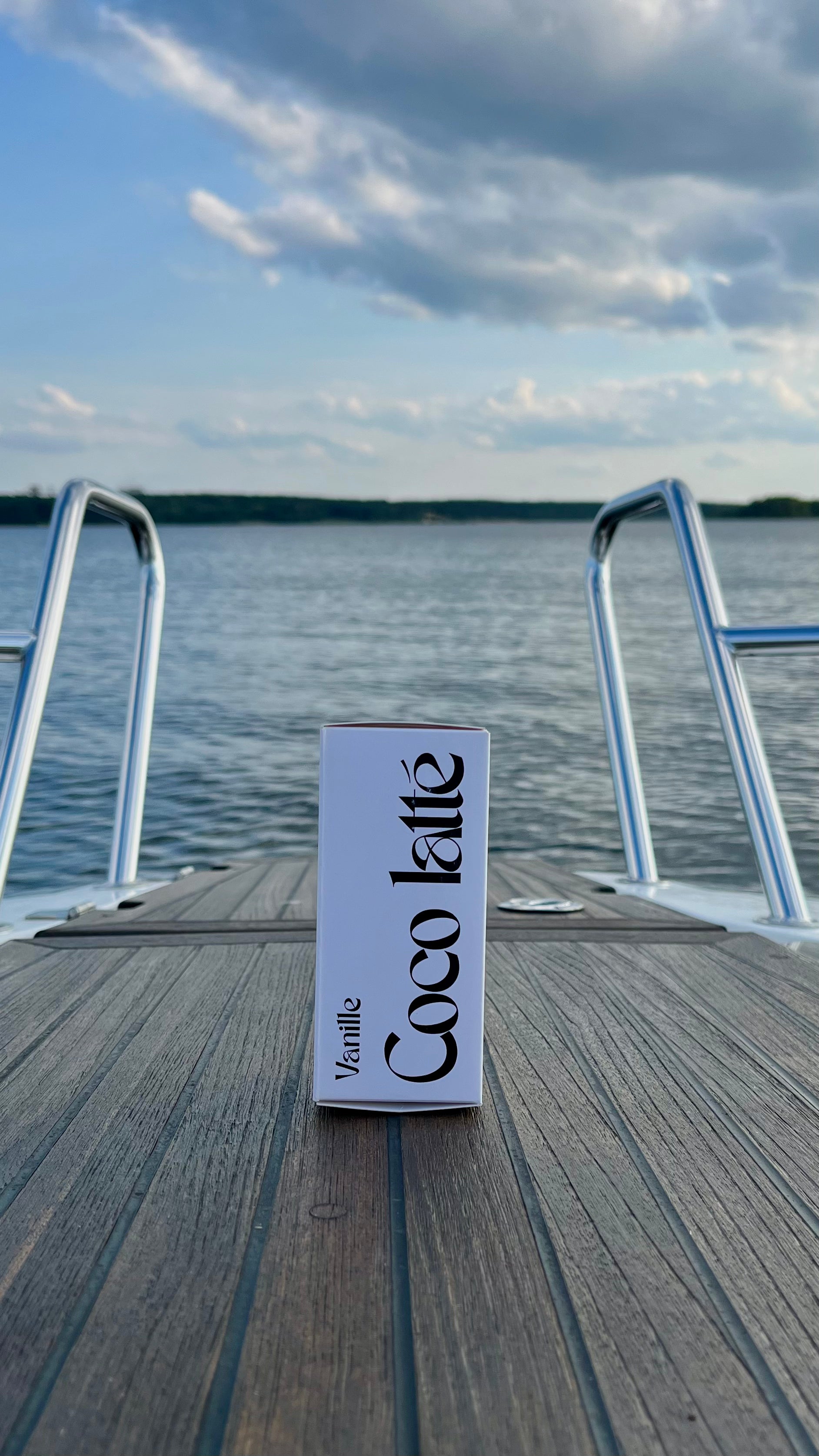 Eau de Toilette Coco latte 100ml. Die Verpackung.  Stehend auf einem Boot im Hintergrund der See mit Wolken.