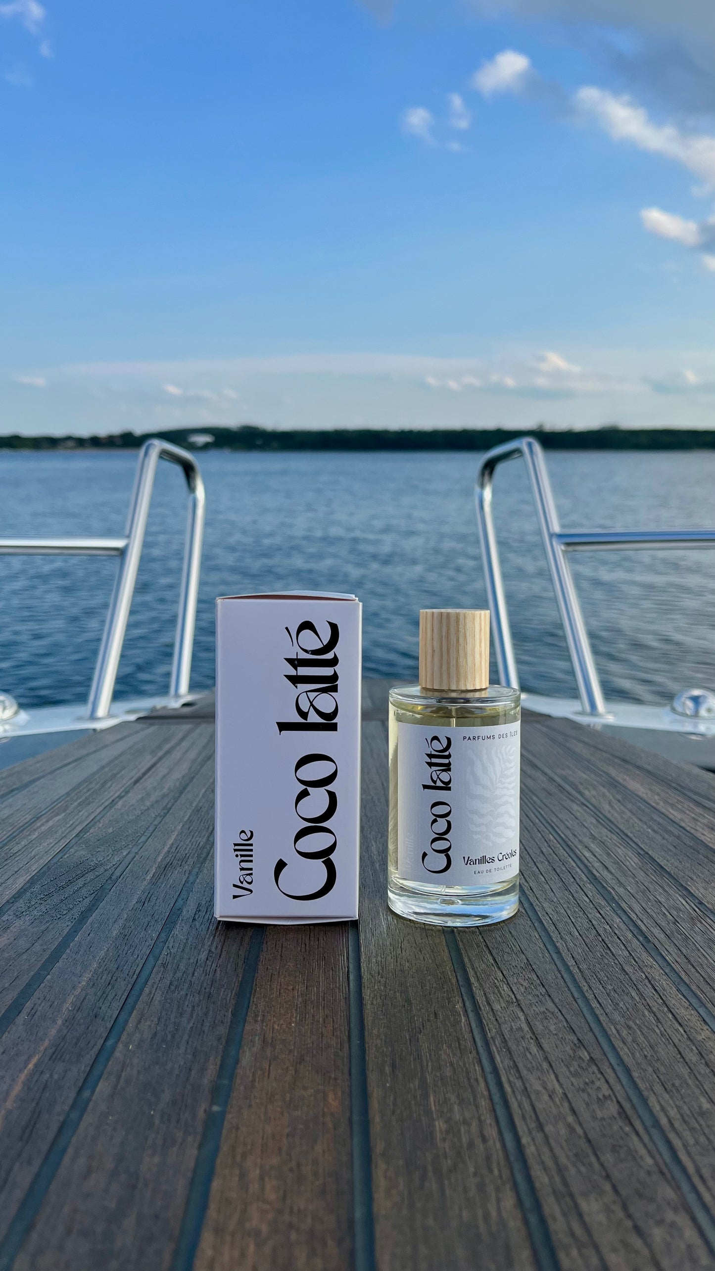 Eau de Toilette Coco Latte 100ml links Karton rechts Flacon. Stehend auf einem Boot im Hintergrund die Reeling und ein See