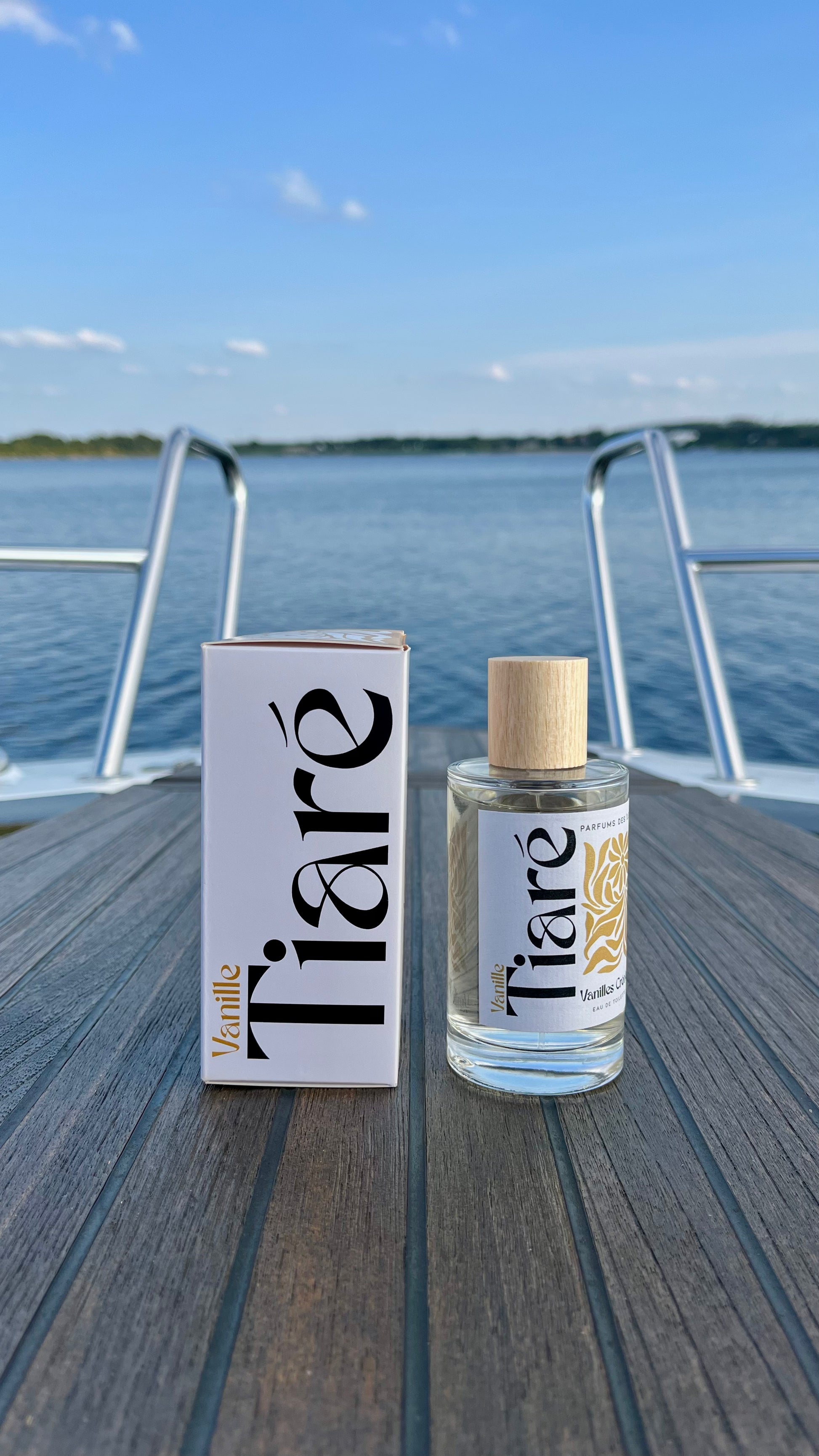 Eau de Toilette Tiare 100ml links Verpackung rechts Flacon. Stehend auf einem Boot im Hintergrund die Reeling und ein See
