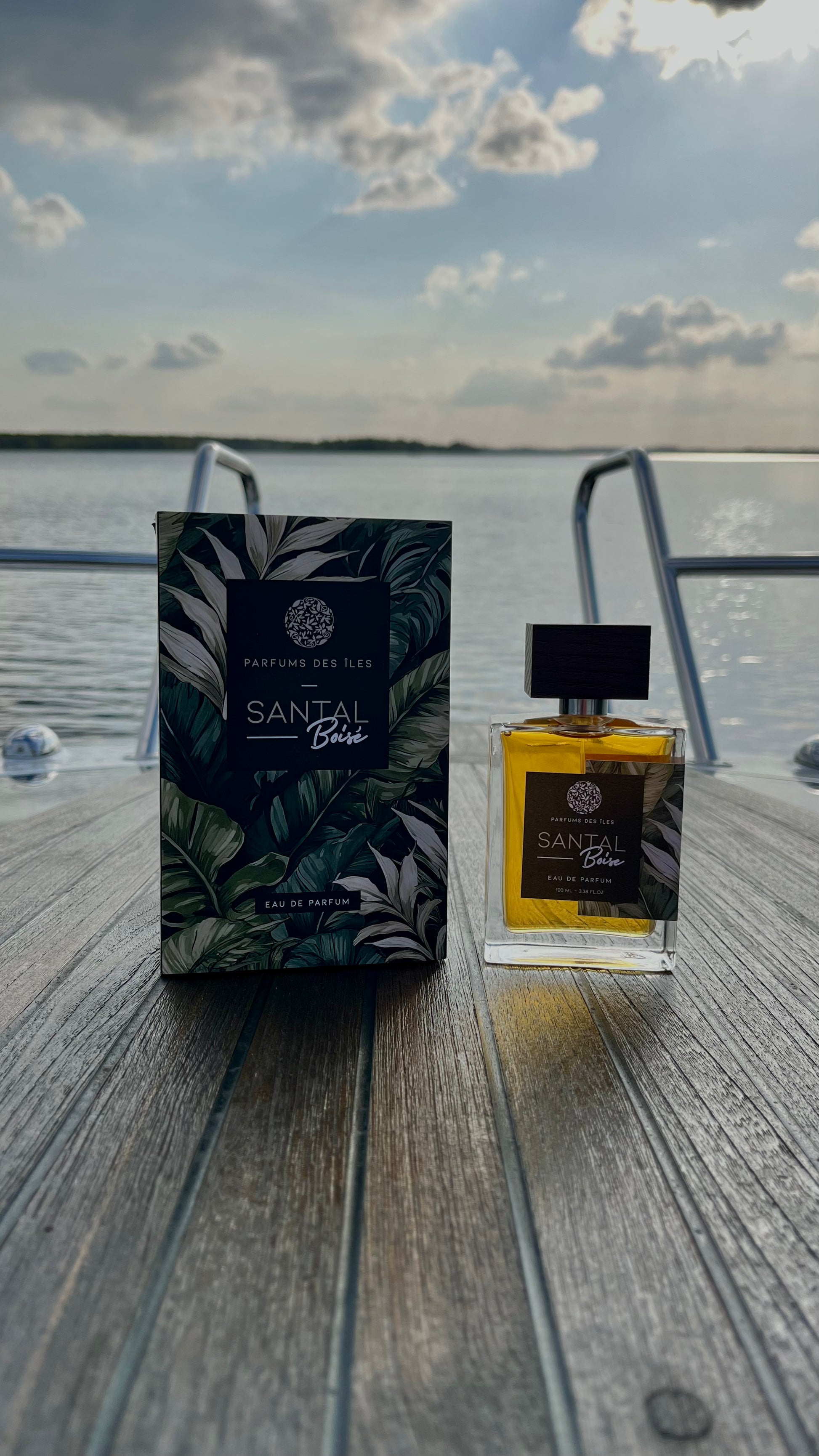 SantalParfüm links Karton rechts Flacon 100ml stehend auf einem Boot. Im Hintergrund die Reeling und der See
