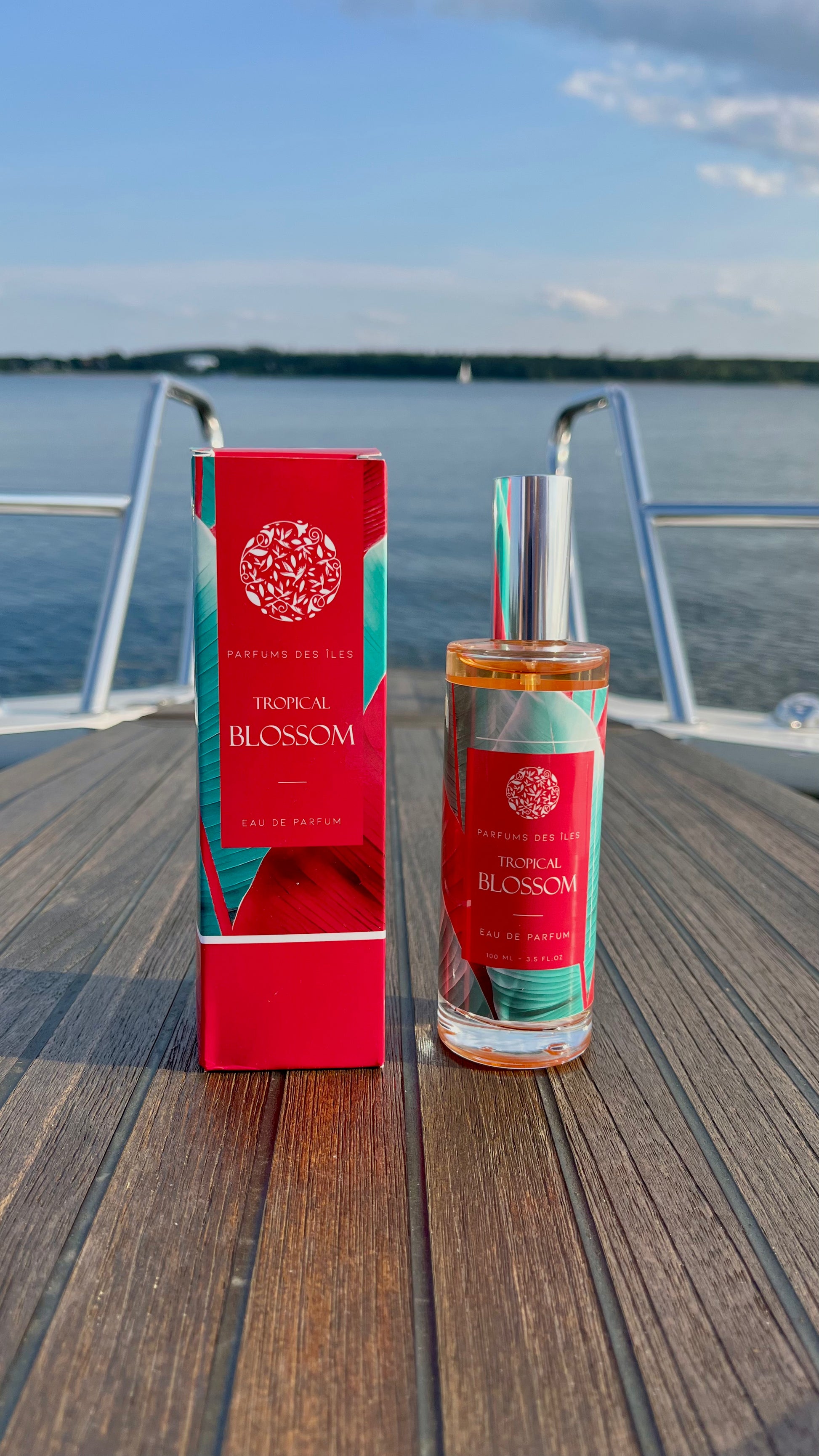 Eau de Parfum Tropical Blossom 100ml links Box, rechts Flacon. Stehend auf einem Boot. Im Hintergrund die Reling und der See