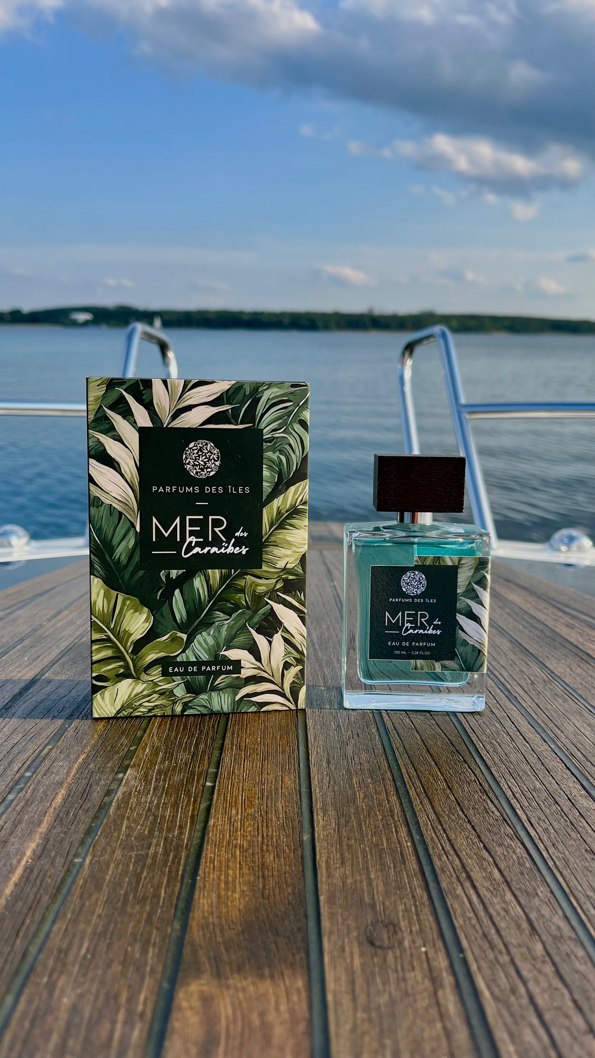 Eau de Parfum Mers des Caraibes 100ml Flacon rechts, links Box, stehend auf einem Boot. Im Hintergrund die Reeling und ein See