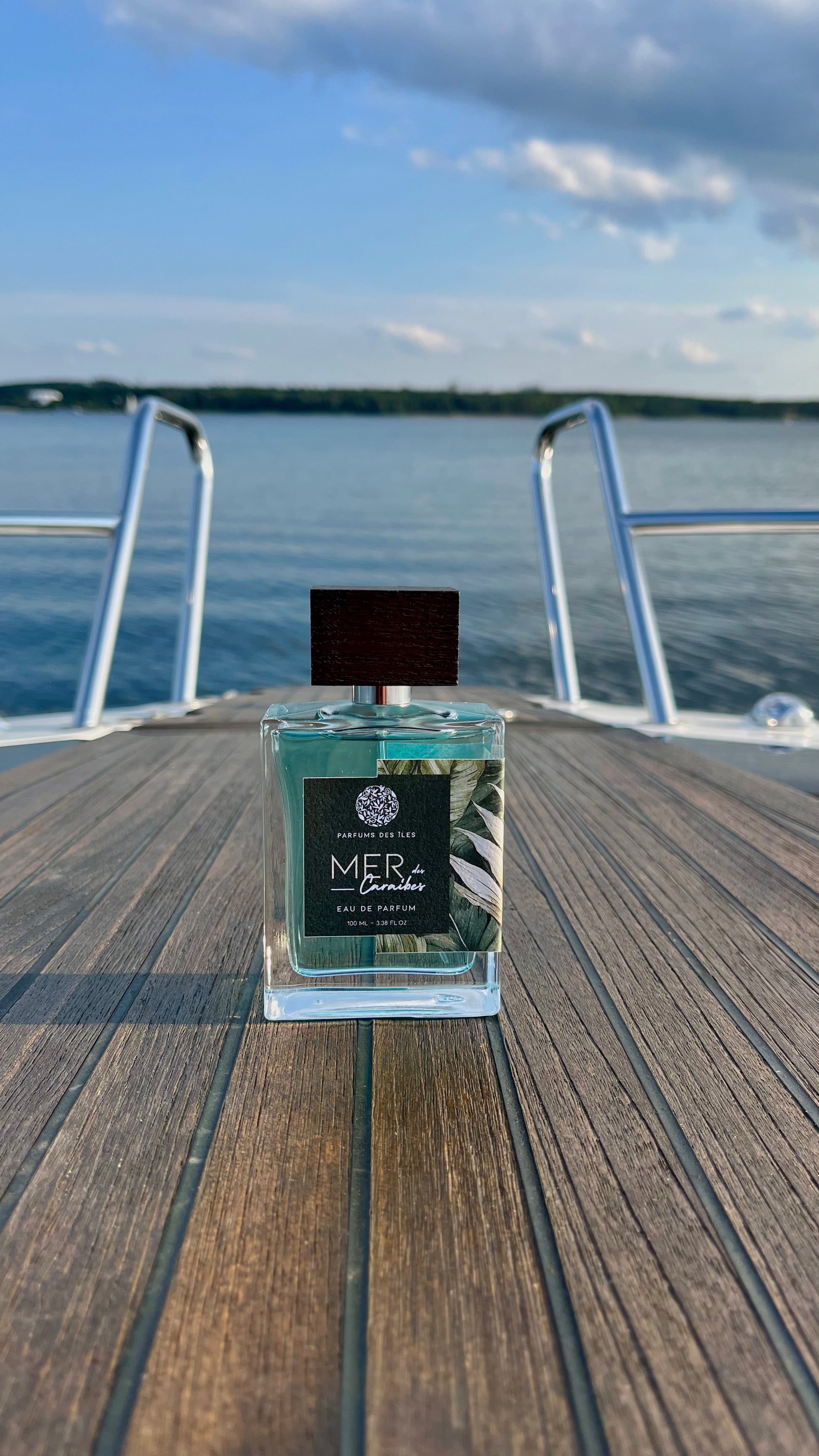Eau de Parfum Mers des Caraibes 100ml Flacon stehend auf einem Boot. Im Hintergrund die Reeling und ein See