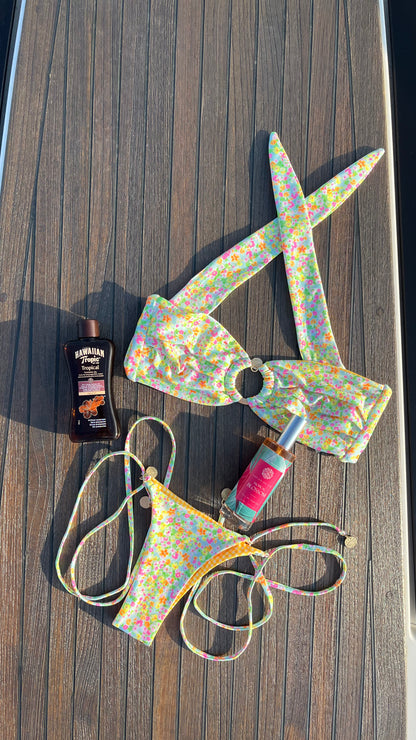 Eau de Parfum Tropical Blossom 100ml Flacon liegend zwischen einem Bunten Bikini auf einem Boot. Links eine Flasche Sonnenschutz