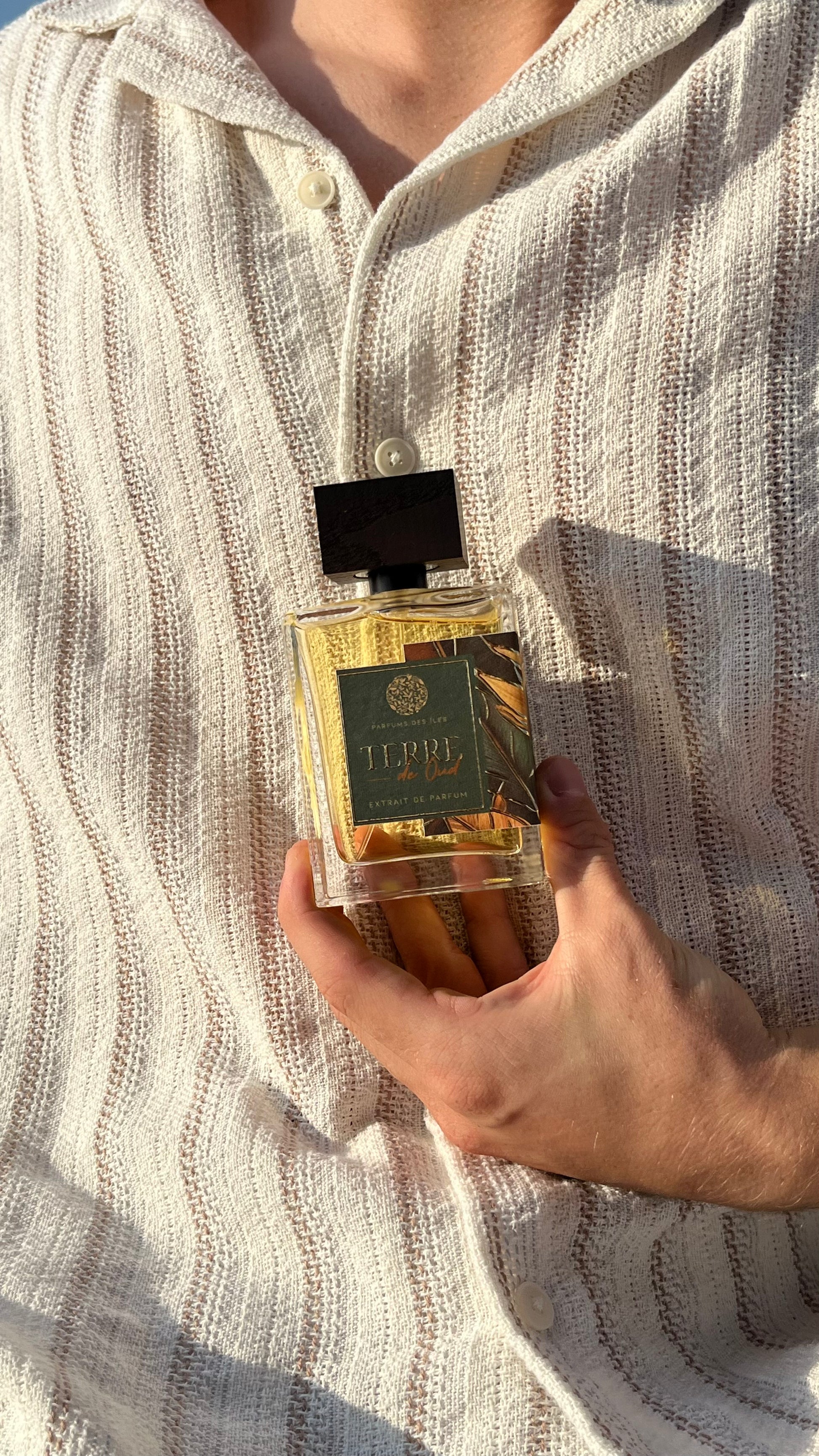 Terre de Oud Parfüm 100ml. Gehalten in der Hand vor dem Körper. Der Körper trägt ein Leinenhemd.
