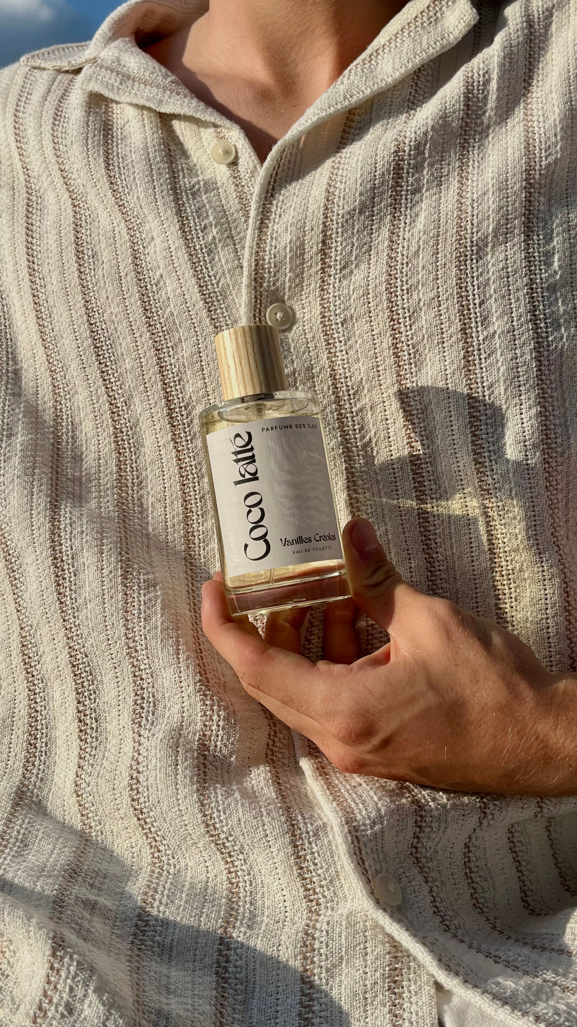 Eau de Toilette Coco latte 100ml. Gehalten in der Hand vor dem Körper. Der Körper trägt ein Leinenhemd.