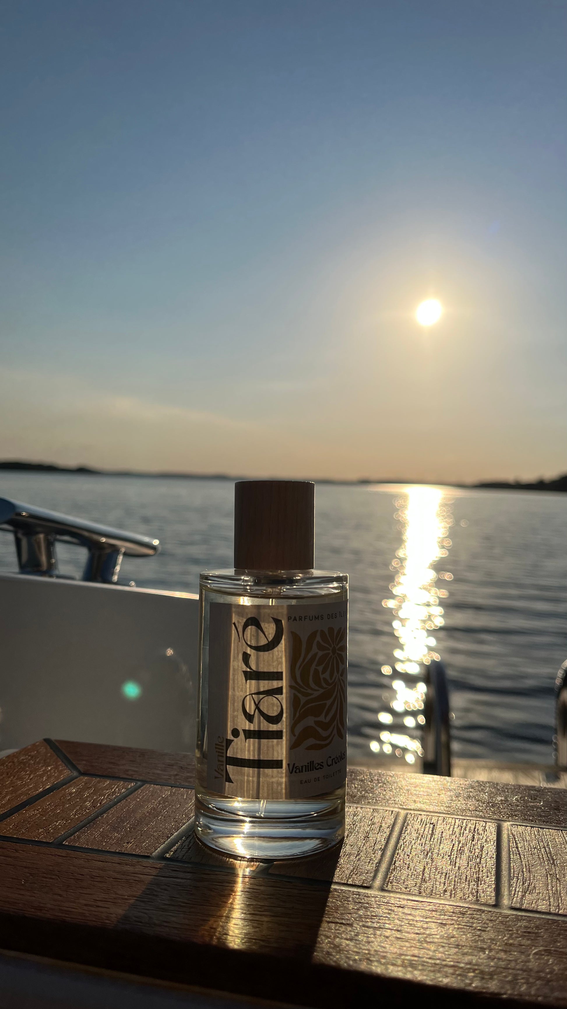 Eau de Toilette Tiare 100ml auf einem Boot stehend. Im Hintergrund ein See und Sonnenuntergang