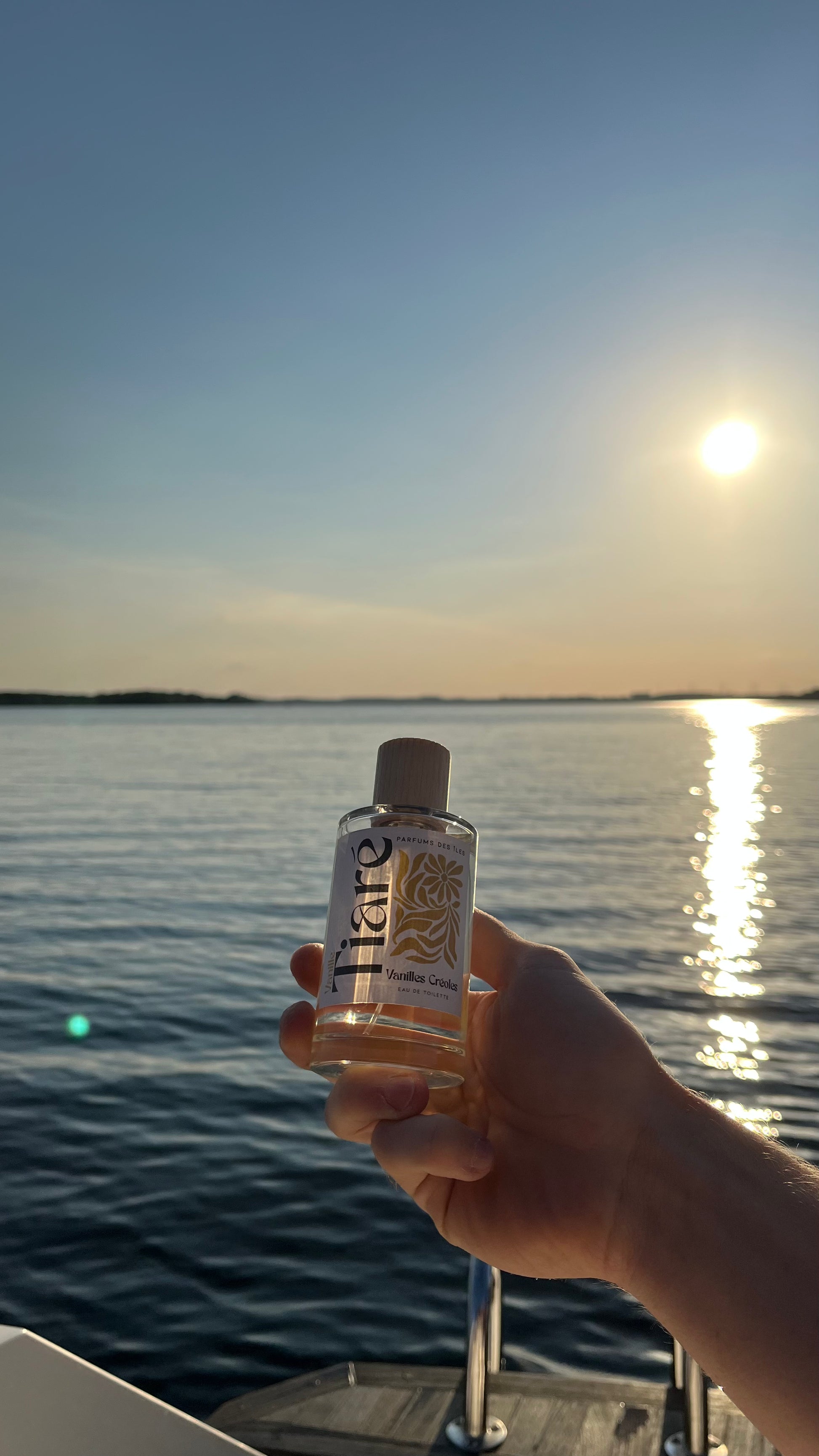 Eau de Toilette Tiare 100ml gehalten in der Hand. Im Hintergrund eine Bootsleiter und See beim Sonnenuntergang