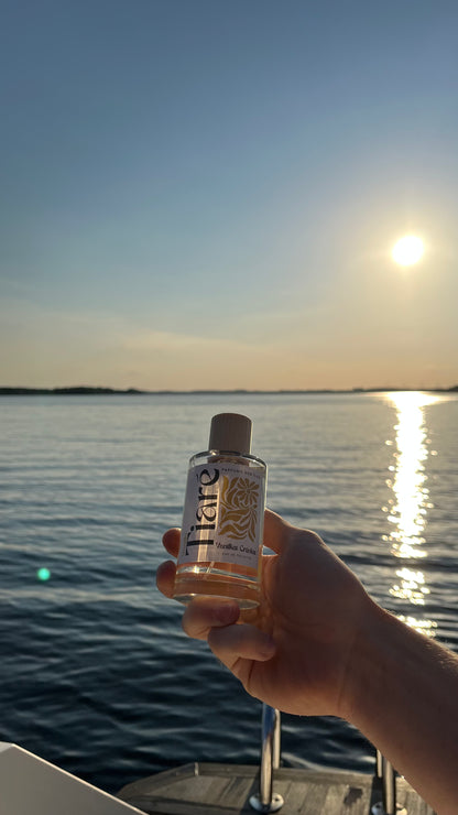 Eau de Toilette Tiare 100ml gehalten in der Hand. Im Hintergrund eine Bootsleiter und See beim Sonnenuntergang