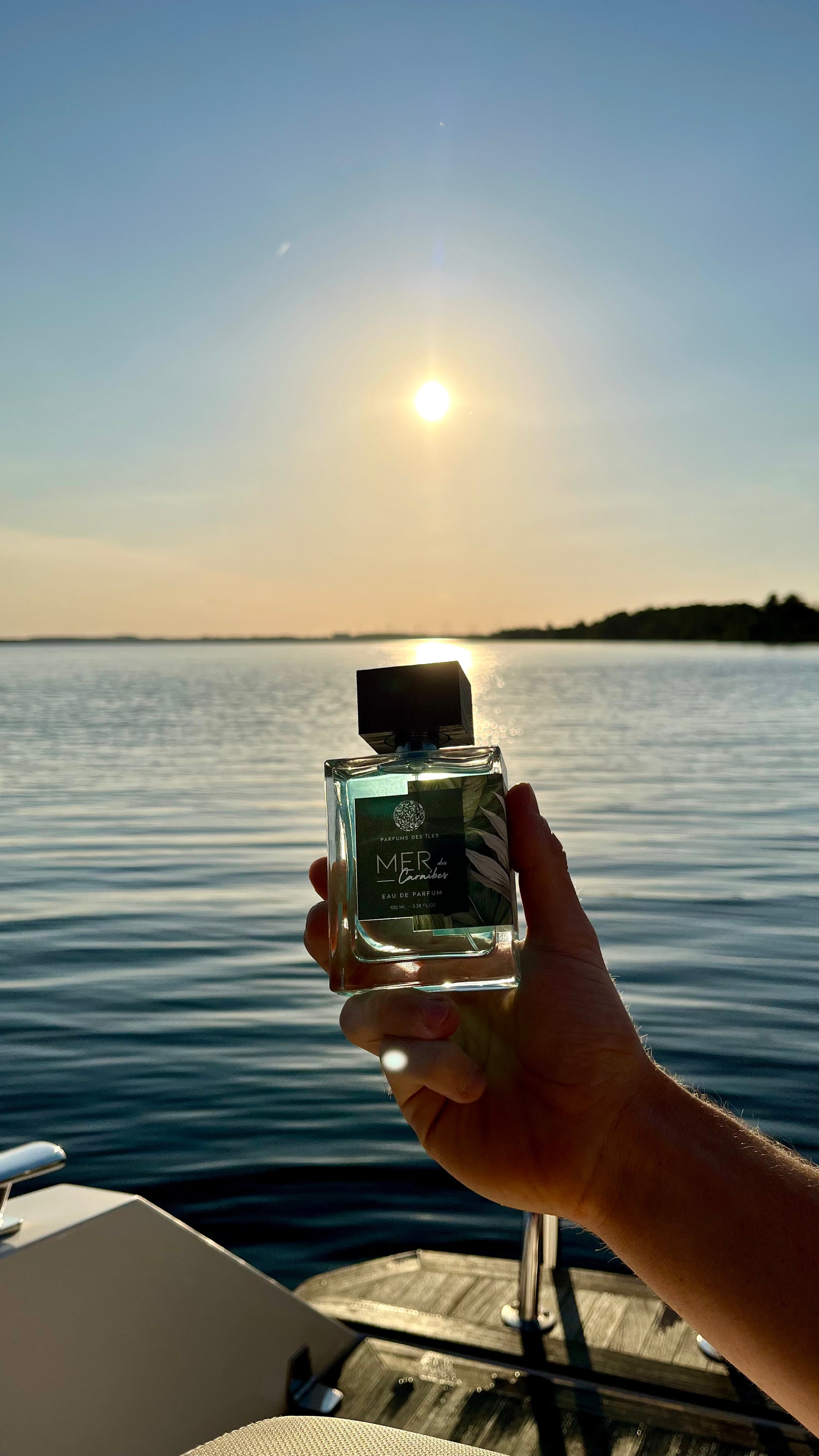 Eau de Parfum Mers des Caraibes 100ml Flacon gehalten in der Hand. Im Hintergrund Wasser im Sonnenuntergang