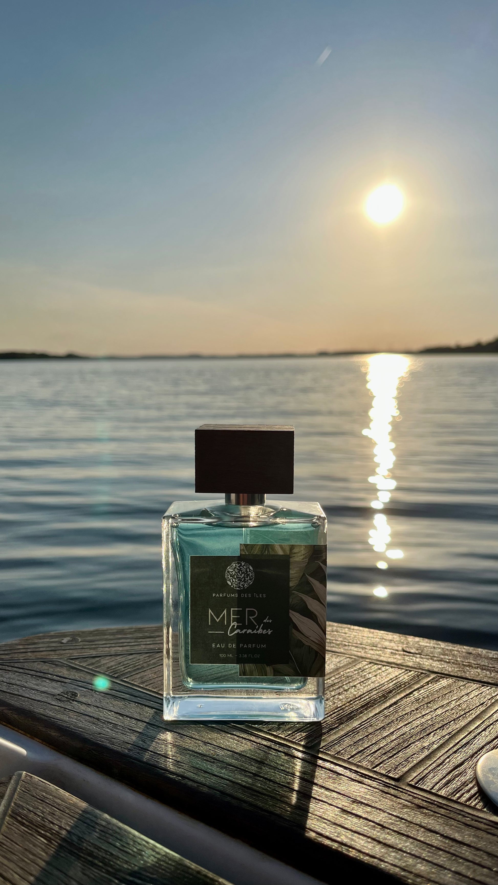 Eau de Parfum Mers des Caraibes 100ml Flacon stehend auf einem Boot. Im Hintergrund das Wasser im Sonnenuntergang