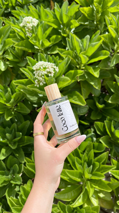 Eau de Toilette Coco latte in der Hand gehalten vor einem Busch