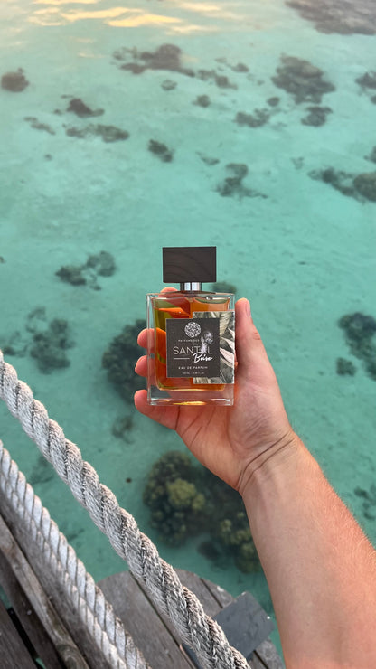 Parfüm Santal gehalten in der Hand auf einem Holzsteg. Im Hintergrund eine türkisfarbene Lagune